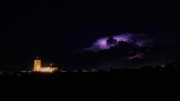 Nit fosca amb una tempesta elèctrica i una església il·luminada al fons.