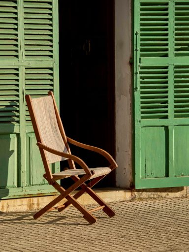 Cadira de fusta plegable davant d'una porta amb persianes verdes.