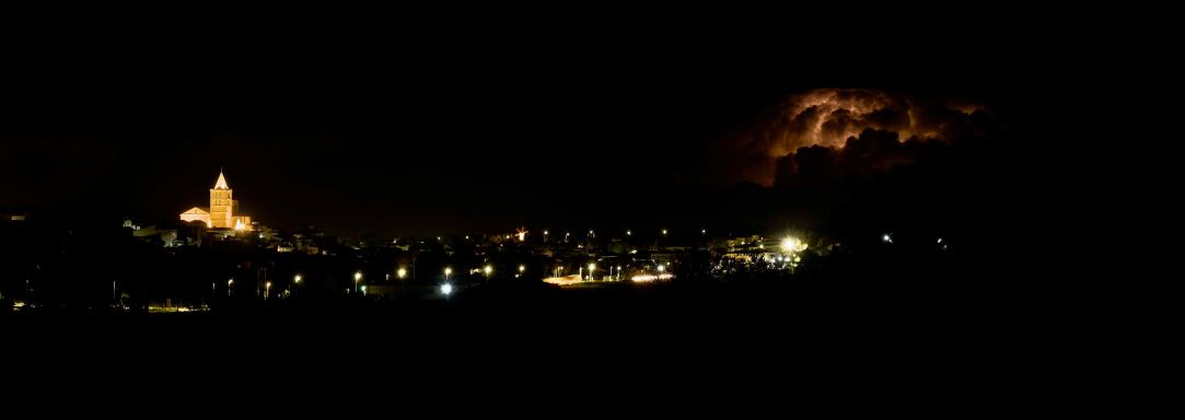 Nit fosca amb una tempesta elèctrica i una església il·luminada al fons.